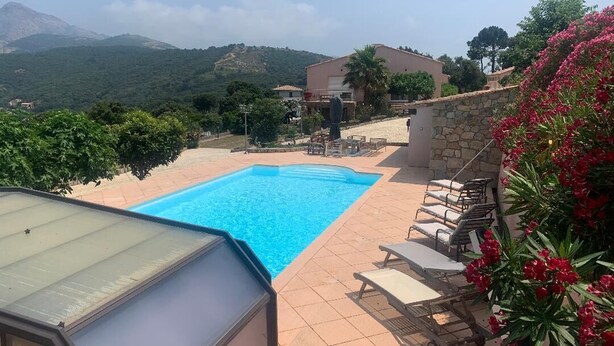 Piscina com espreguiçadeiras e área coberta, cercada por muros de pedra e vegetação, com vista para colinas ao fundo.
