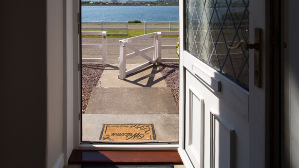 Uma porta dá para uma varanda com vista para um lago e colinas ao longe.