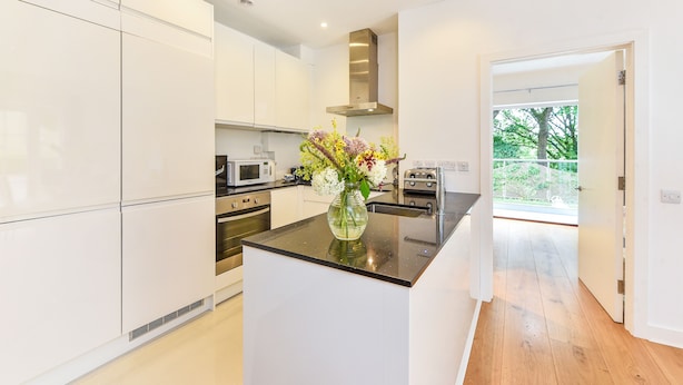 Una cocina moderna con armarios blancos, una isla central y vistas al exterior.