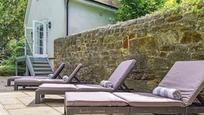 Un conjunto de sillones de exterior con cojines, un muro de piedra y una escalera que conduce a un edificio.