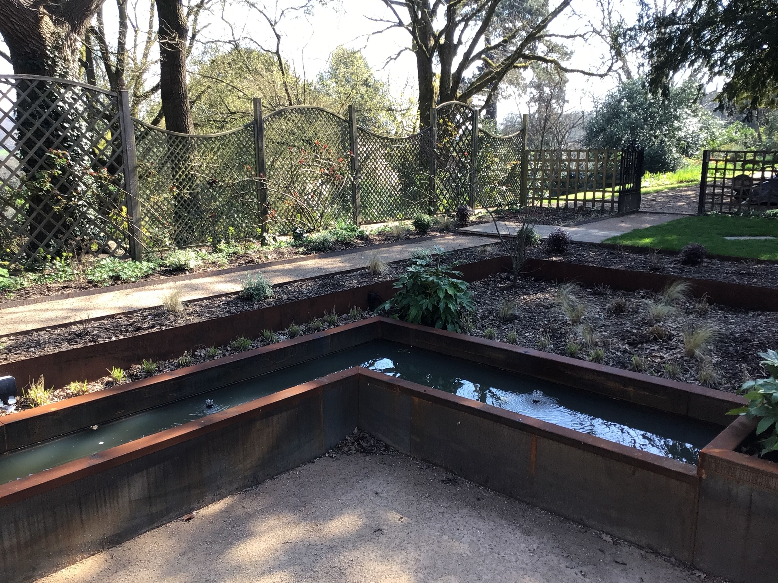 Un jardin agrémenté d’un élément aquatique, de clôtures en métal et d’un sentier.