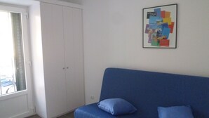 Ett rum med en blå soffa, två kuddar, en vit garderob och en inramad tavla på väggen.