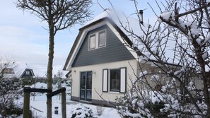 Une maison moderne à deux étages, dotée d’un toit en pente, d’une cheminée visible et d’une porte d’entrée avec un panneau de verre.