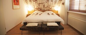Une chambre à coucher avec une tête de lit en bois, deux lampes de chevet, un lit avec une literie blanche et un banc au pied du lit.