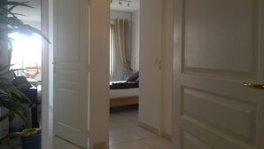 Quarto com cama, janela com cortinas, uma planta e porta para outro cômodo.