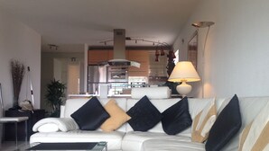 Uma sala de estar moderna com um sofá branco, uma mesa de centro de vidro e uma luminária.