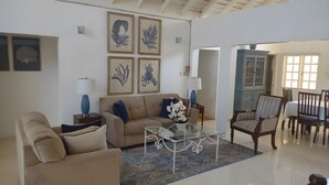 A living room with a beige sofa, a glass coffee table, and a patterned rug. There are framed botanical prints on the wall and a blue vase on the side table. - The beautuful Butterfly Villa situated in the exclusive Silver Sands estate (Duncans)