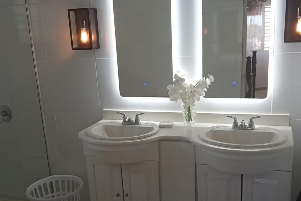 A bathroom with two sinks, a large mirror, and a vase with flowers.