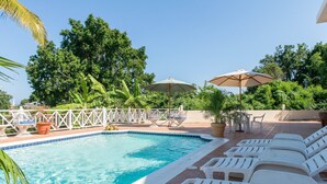A swimming pool with lounge chairs and umbrellas, surrounded by greenery and a white fence. - The beautuful Butterfly Villa situated in the exclusive Silver Sands estate (Duncans)