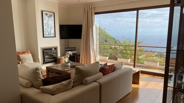 A living room with a sofa, TV, and a balcony with a view of the sea. -  Spacious villa,  180* ocean view, large heated pool, 5 min from Calheta beach (Calheta)