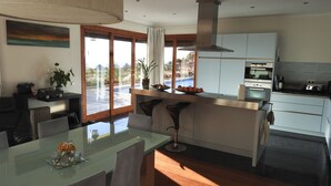 A modern kitchen with a large island, a dining area with a glass table, and a view of the outdoors. -  Spacious villa,  180* ocean view, large heated pool, 5 min from Calheta beach (Calheta)