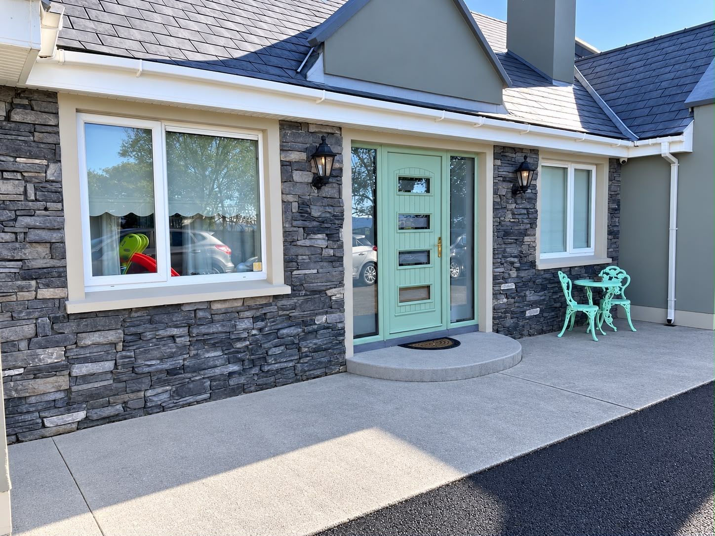A house with a stone facade, a green door, and a small patio with two chairs.