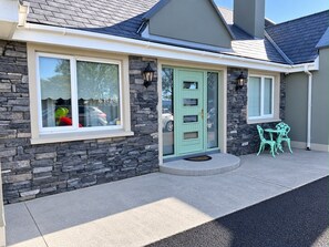 A house with a stone facade, a green door, and a small patio with two chairs. - Luxurious Modern Country House in private area with stunning views of Killarney  (Killarney)