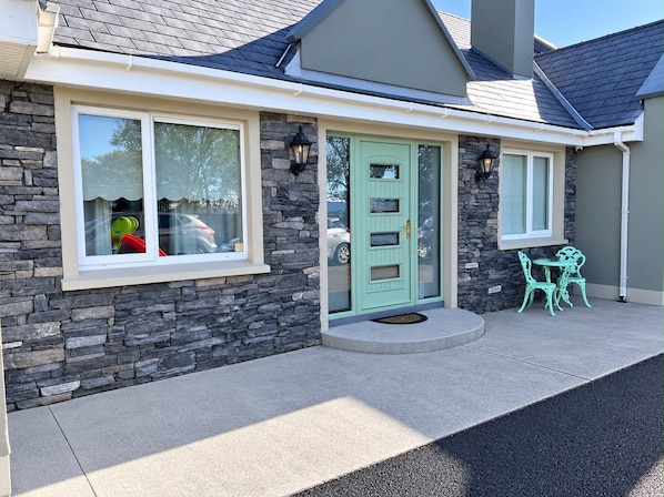A house with a stone facade, a green door, and a small patio with two chairs.
