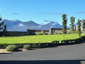 A paved driveway leading to a building with a well-maintained lawn and a mountain in the background.