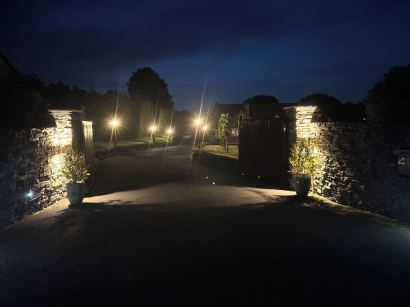 A gated entrance with stone walls and potted plants, illuminated by street lamps.