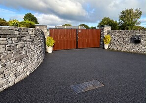 A gated entrance with a stone wall, a metal gate, and a paved driveway.