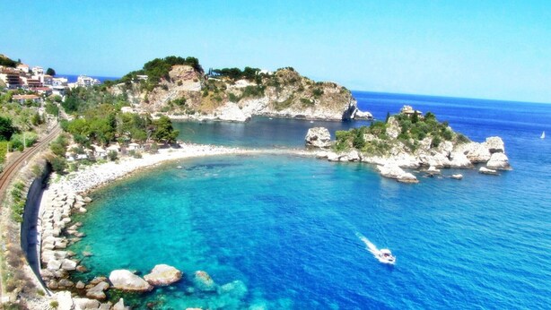 A coastal area with a clear blue sea, rocky shoreline, and a small boat.