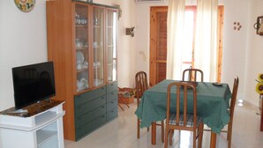 A dining area with a table set for four, a television on a stand, and a cabinet with glass doors.
