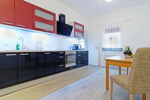 A modern kitchen with black and red cabinets, a built-in oven, and a dining area with a table and chair.