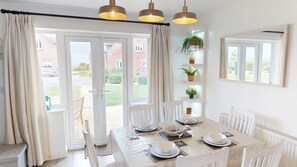 A dining area with a table set for four, a window with curtains, and a plant on a shelf. - Sea Urchins Cottage -  a cottage that sleeps 5 guests  in 2 bedrooms (Filey)
