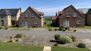 A row of brick houses with pitched roofs, a paved driveway, and a grassy area with small shrubs. - Sea Urchins Cottage -  a cottage that sleeps 5 guests  in 2 bedrooms (Filey)