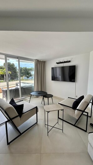 Un salon moderne comprenant un canapé, deux fauteuils, une petite table, un téléviseur à écran plat fixé au mur et une porte-fenêtre coulissante donnant sur un espace extérieur.