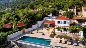 Eine moderne Villa mit Swimmingpool, umgeben von üppiger Vegetation und Bergen.
