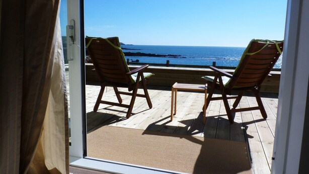 A balcony with two wooden chairs and a small table, overlooking a body of water. - A very special place (Co. Cork)