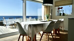 A dining area with a table set for four, overlooking a deck with chairs, a large window with a view of the sea, and a hanging lamp. - A very special place (Co. Cork)