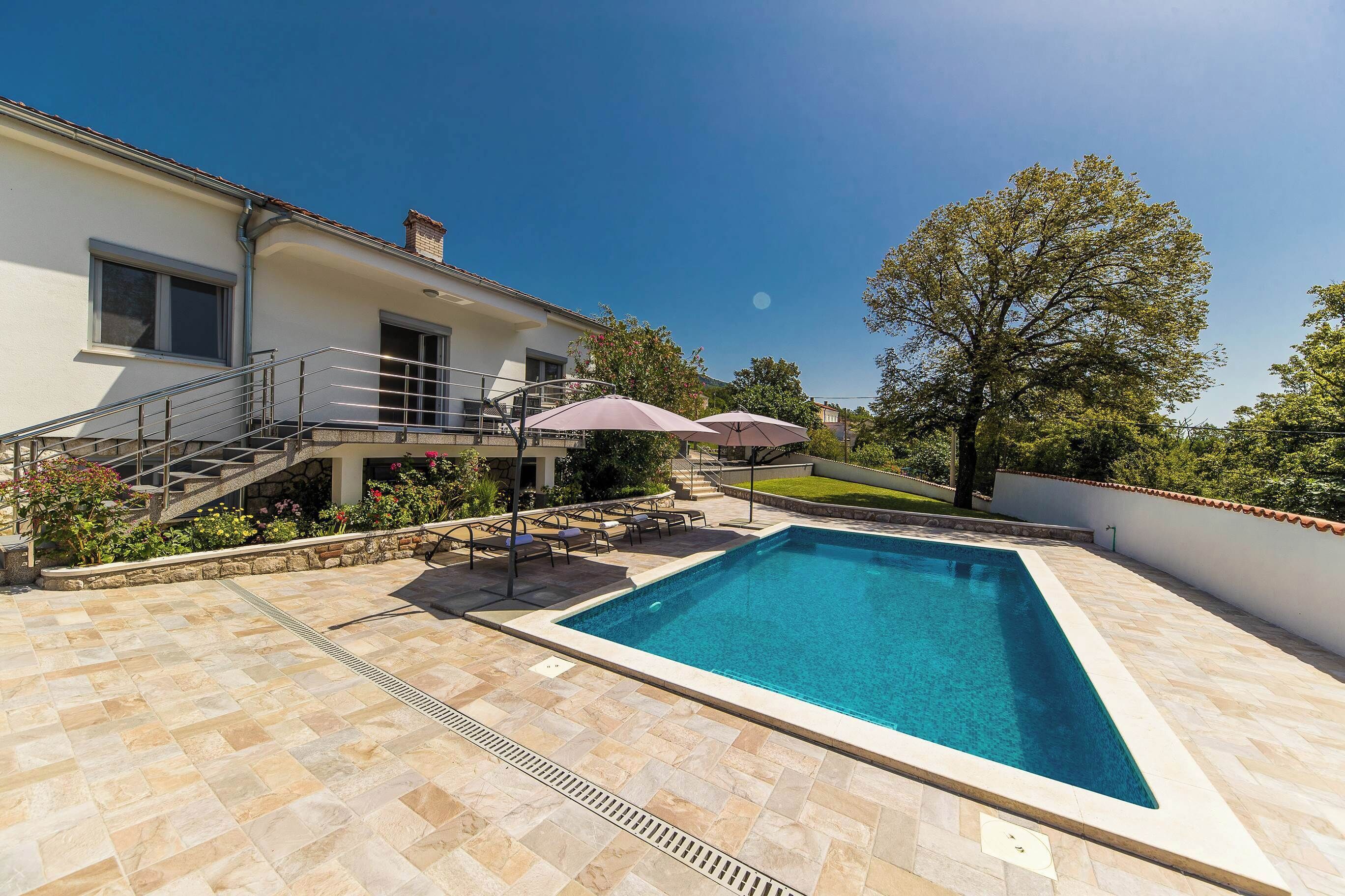 A swimming pool with a stone deck, a covered outdoor seating area, and a staircase leading to a second floor.