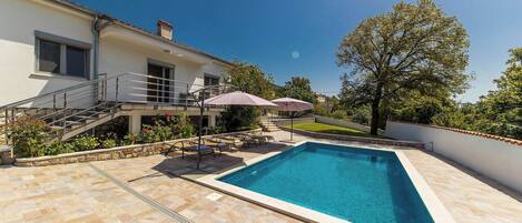 A swimming pool with a stone deck, a covered outdoor seating area, and a staircase leading to a second floor.