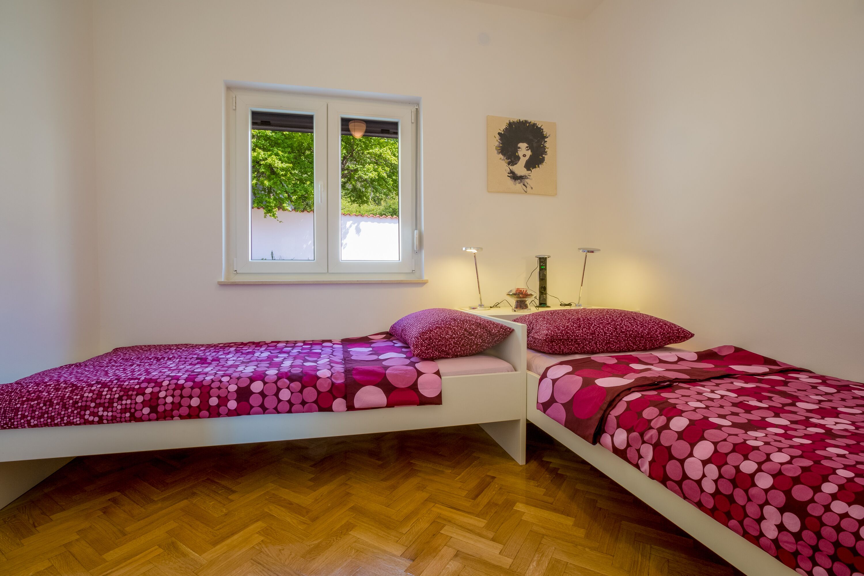Een slaapkamer met twee eenpersoonsbedden, een raam met uitzicht op bomen, een kunstwerk aan de muur en een nachtkastje met een lamp.