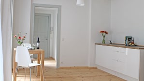 Une cuisine moderne avec un plancher en bois, des meubles blancs et un coin repas comprenant une table et des chaises blanches.