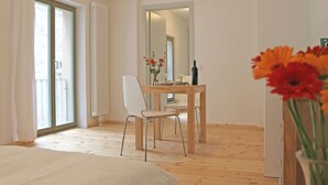 Une pièce comprenant un lit, une table à manger en bois avec des chaises, un miroir et un vase avec des fleurs.