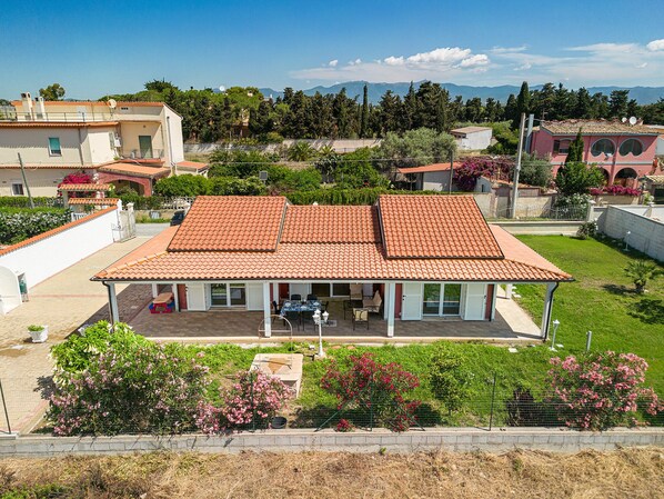 A two-story house with a tiled roof, a covered patio, and a garden with flowering plants.