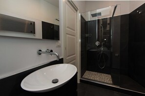Ein modernes Badezimmer mit einem weißen Waschbecken, einer Duschkabine aus Glas und einem schwarzen Fliesenboden.