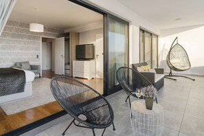 Een moderne woonkamer met een bank, twee zwarte draadstoelen, een kleine ronde tafel met een vaas, en een televisie op de achtergrond.