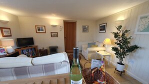 A living room with a sofa, a television, a bookshelf, a potted plant, and a bottle of wine. - Country Cottage Set In pretty Suffolk village with 2 local pubs, dog friendly (Lower Ufford)