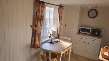 Uma cozinha com mesa de madeira, armários brancos, micro-ondas e relógio na parede.