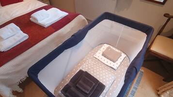 Ein Hotelzimmer mit zwei Betten, eines mit einer rot-weißen Tagesdecke und das andere mit einer blau-weißen. Ein Fenster mit Vorhängen, ein Heizkörper und ein kleiner Tisch mit Lampe und Büchern sind ebenfalls vorhanden.