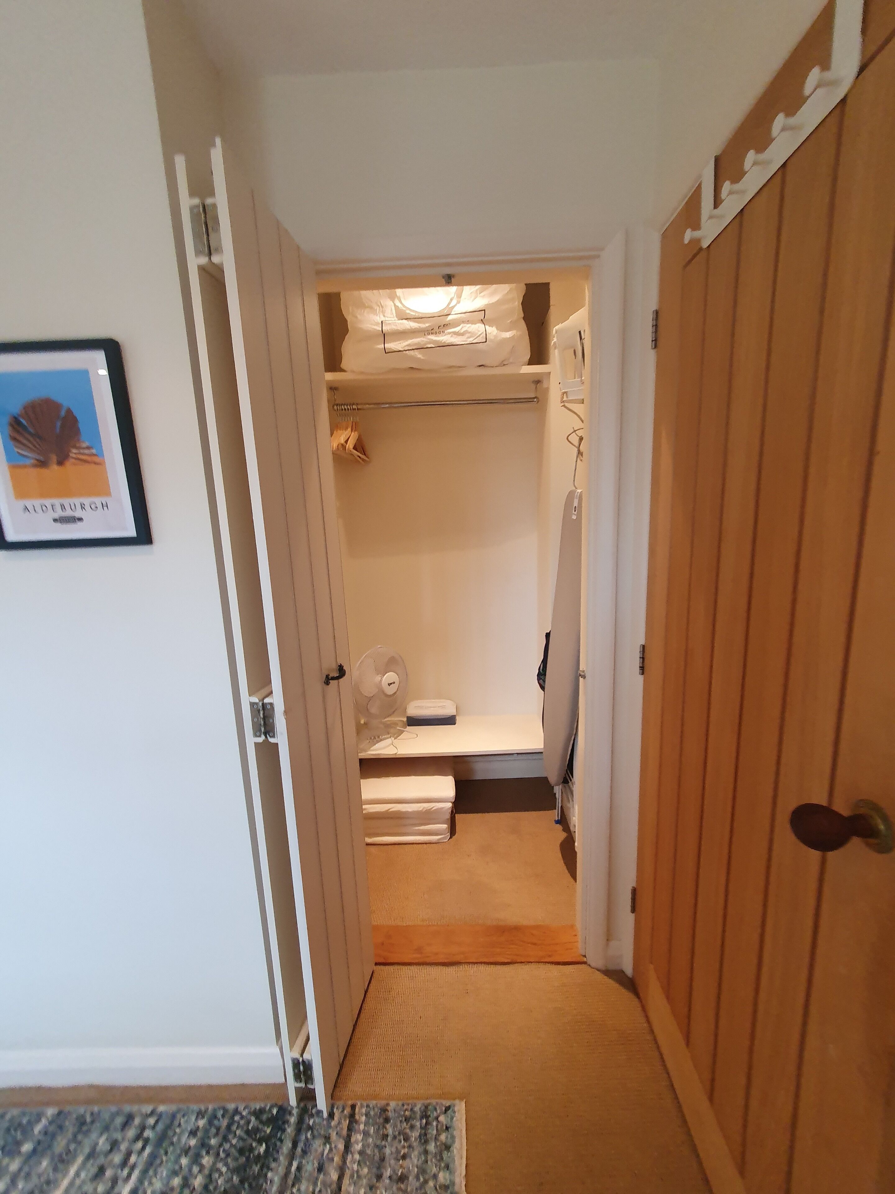 Un corridoio che conduce a una cabina armadio con un letto, una ventola e un quadro appeso al muro.