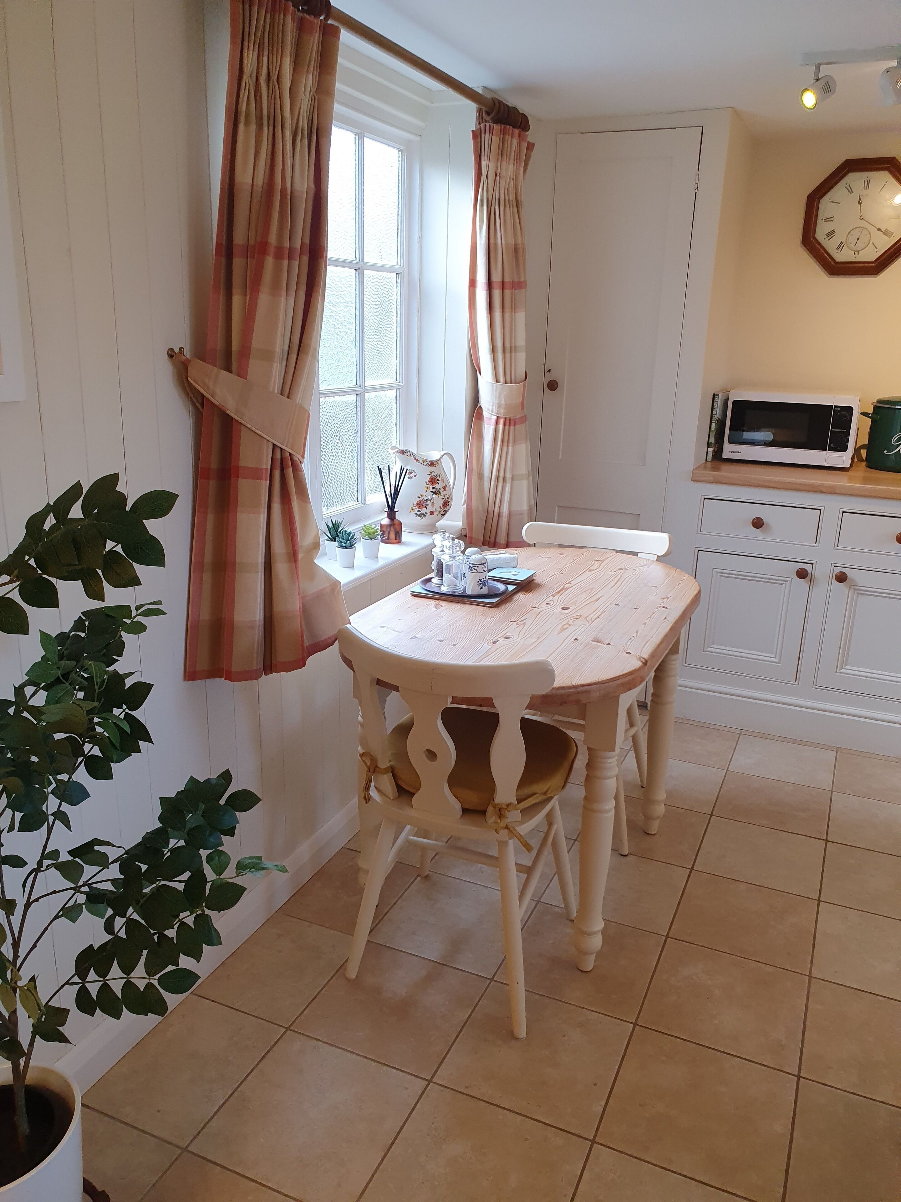 A cozy kitchen with a wooden table, a microwave, and a clock on the wall.
