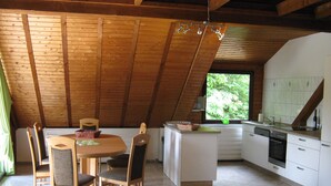 A kitchen with a dining area, wooden ceiling beams, and a view of greenery outside. - Cozy, comfortably furnished apartment for up to 7 people with balcony (Immerath)