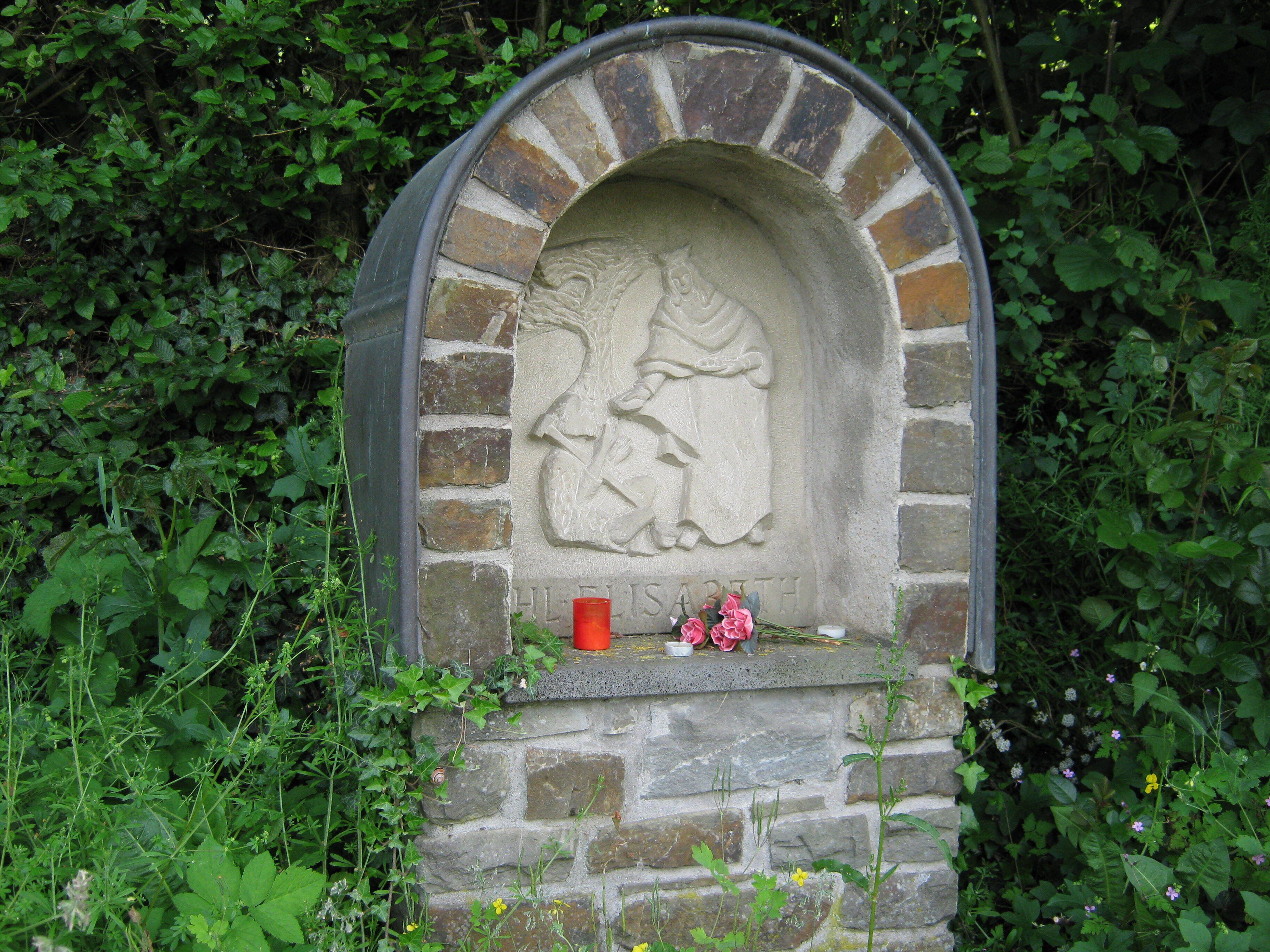 A stone memorial with a carved figure, surrounded by greenery.