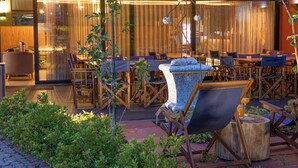 An outdoor dining area with wooden tables and chairs, a stone planter, and a wooden deck. - S. Torcato Valley Houses - House 1 (Guimarães)