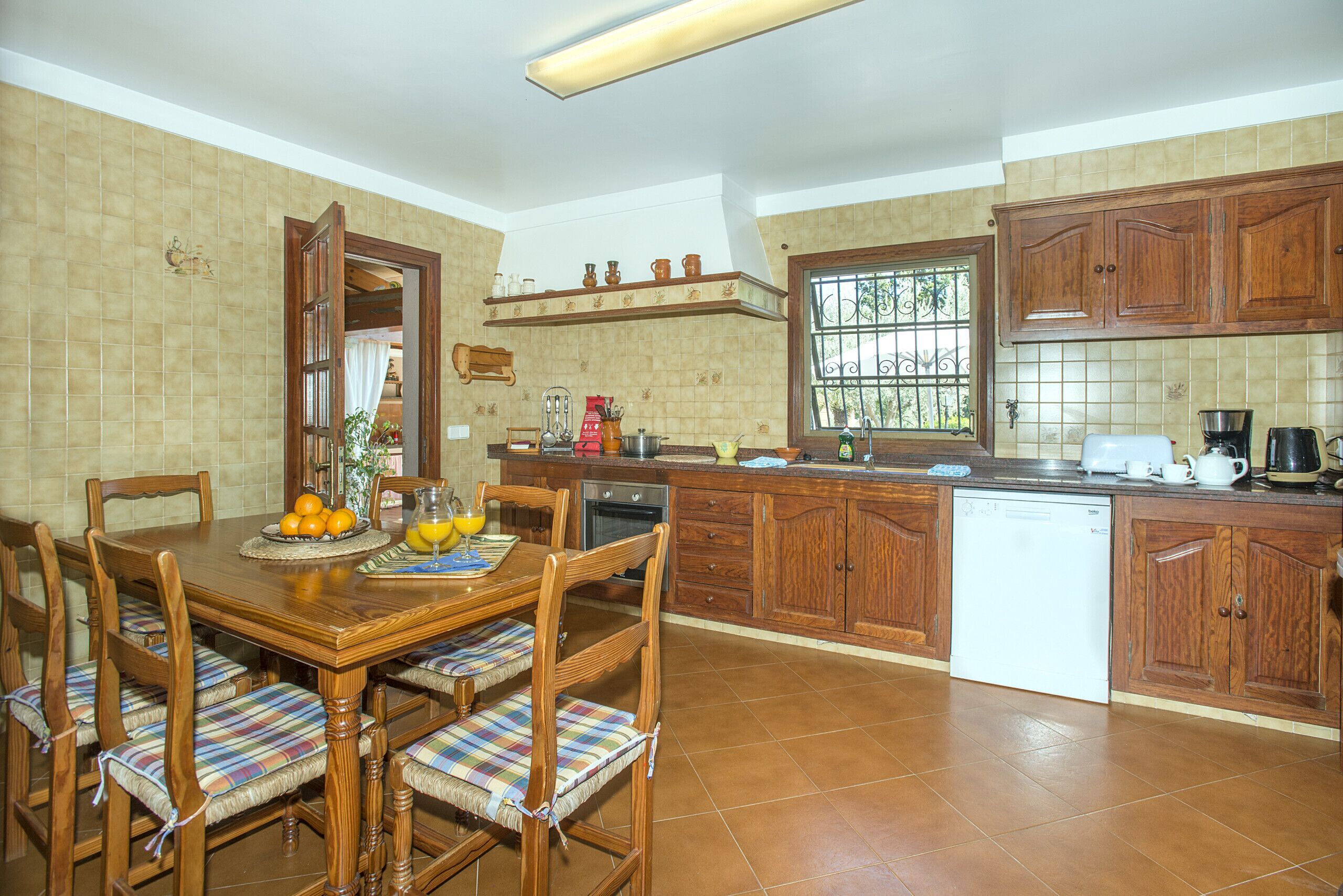 Una cocina con armarios de madera, una mesa de comedor con sillas y un ventanal con barrotes.