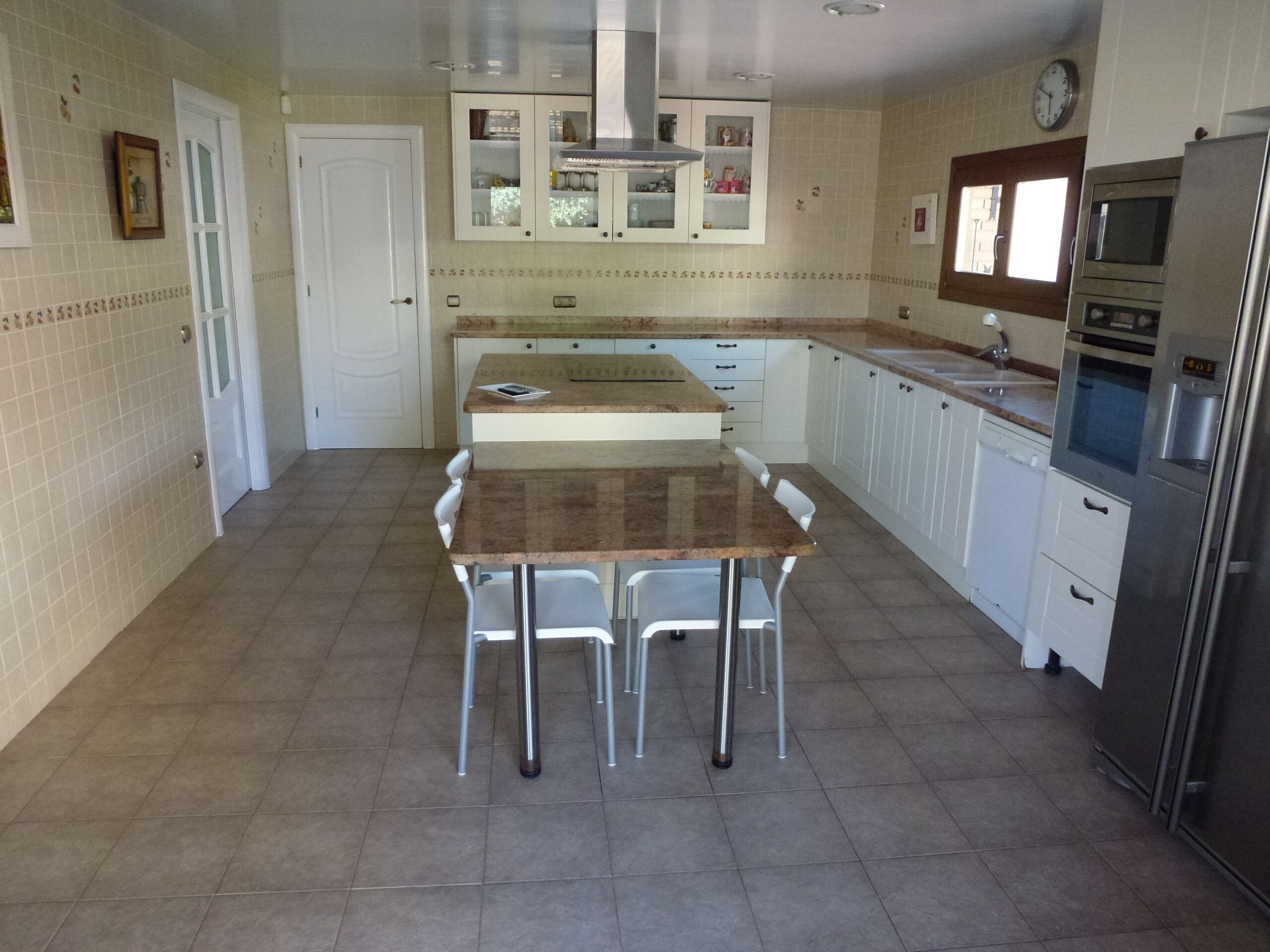 Una cocina con una isla central, armarios blancos y electrodomésticos de acero inoxidable.