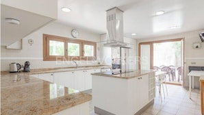 Een moderne keuken met witte kasten, een granieten aanrecht en een centraal eiland. Er is een raam boven de spoelbak en een klok aan de muur.