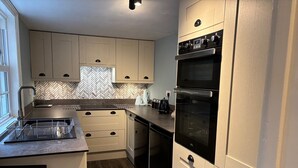 A modern kitchen with light-colored cabinets, a herringbone-patterned backsplash, a built-in oven, and a dishwasher. - Spacious 3 bed holiday cottage in Hunstanton only 150 metres to the beach. (Hunstanton)